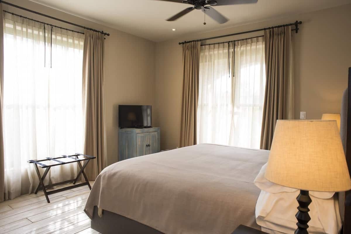 Une chambre d’hôtel avec un lit, une télévision, un ventilateur de plafond et une fenêtre avec des rideaux.