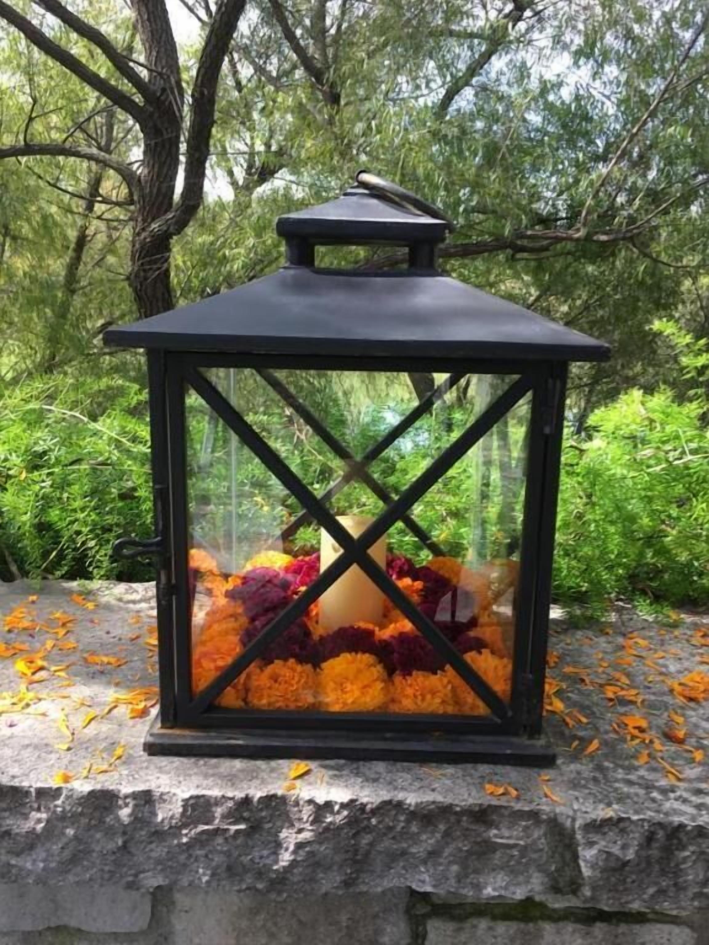 A lantern with a black frame and glass panels, placed on a stone ledge surrounded by autumn leaves.