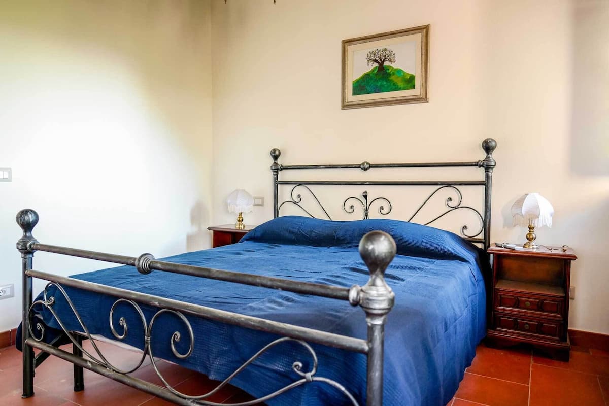 A bed with a metal frame, blue bedding, two bedside tables with lamps, and a painting on the wall.