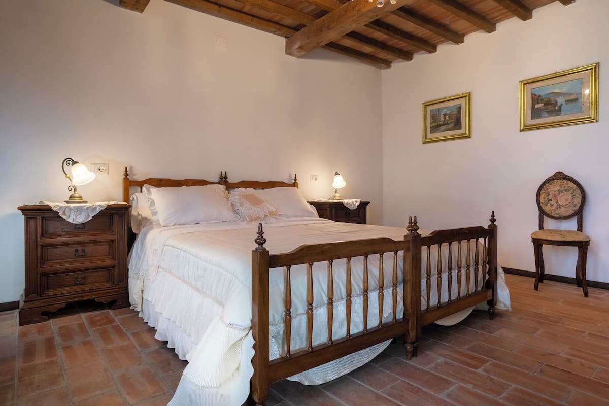 A bedroom with a wooden bed, two bedside tables with lamps, a nightstand, and a chair.