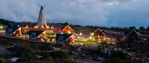 Une série de chalets en bois, avec un moulin à vent bien visible, nichés dans un paysage naturel au crépuscule.