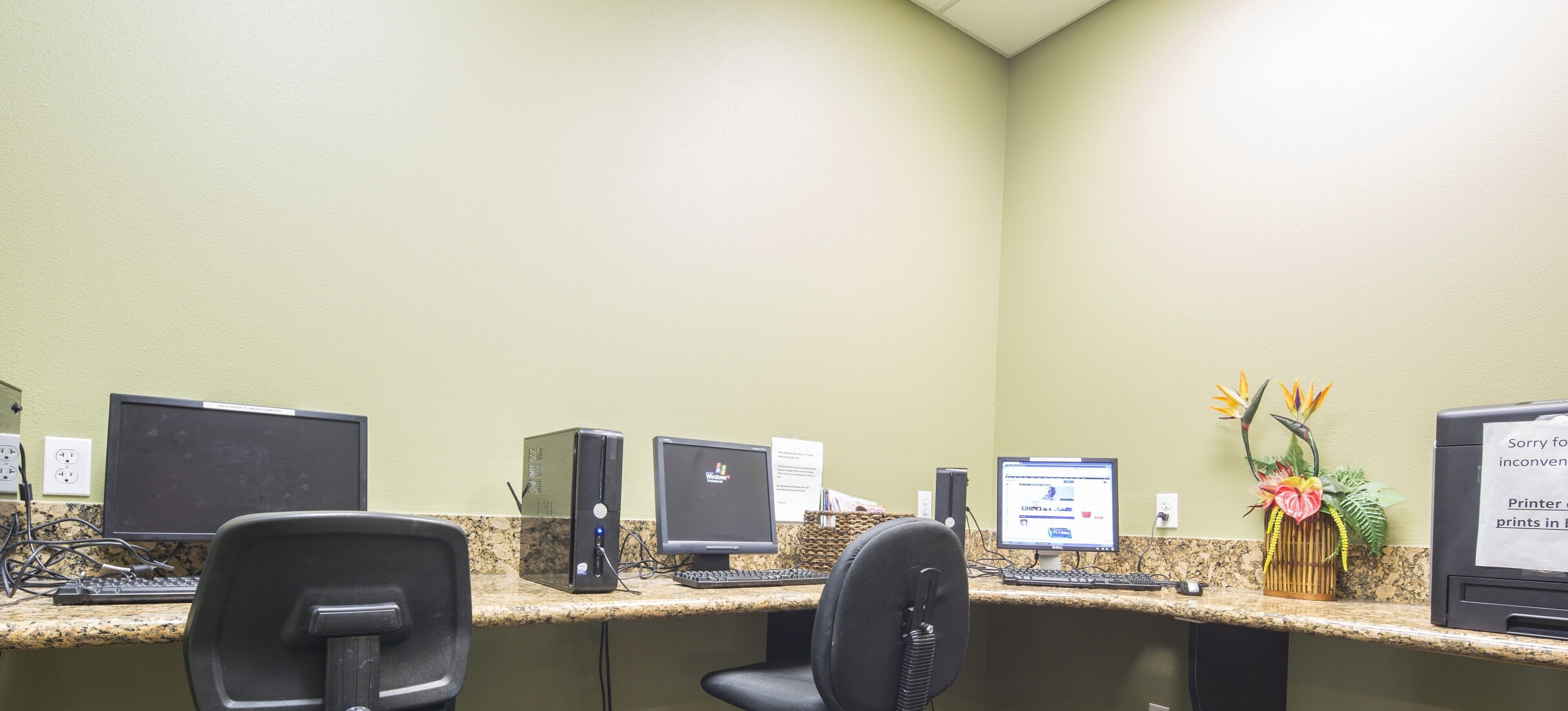Un espace d’accueil comprenant plusieurs postes de travail équipés d’ordinateurs, une imprimante et une plante décorative.