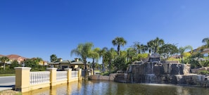 A water feature with cascading water over rocks, surrounded by a fence and palm trees.