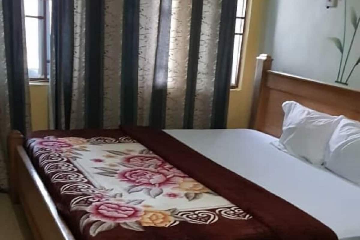 A single bed with a floral bedspread, a wooden headboard, and a nightstand with a lamp.