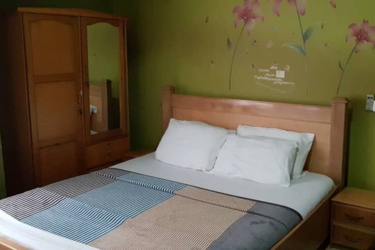 A bedroom with a bed, a nightstand, a green armchair, and a wardrobe.