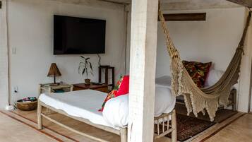 Quarto com cama, rede, televisão e uma pequena mesa com abajur.