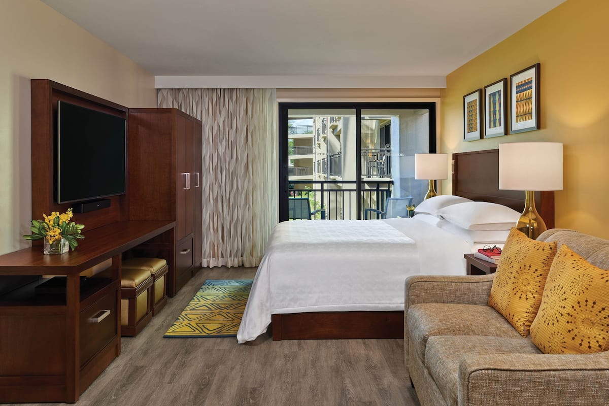 Habitación de hotel con una cama grande, televisor, sofá y balcón con vistas.