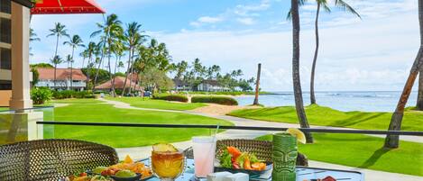 A table set with food and drinks, overlooking a golf course and the ocean.