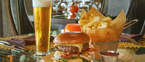 A meal consisting of a burger, fries, and a beer on a table with a woven placemat.
