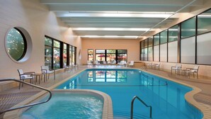 Una piscina interior con suelo de baldosas, un jacuzzi y sillas de descanso alrededor.