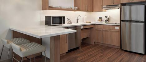 A modern kitchen with wooden cabinets, a stainless steel refrigerator, a microwave, and a bar stool.