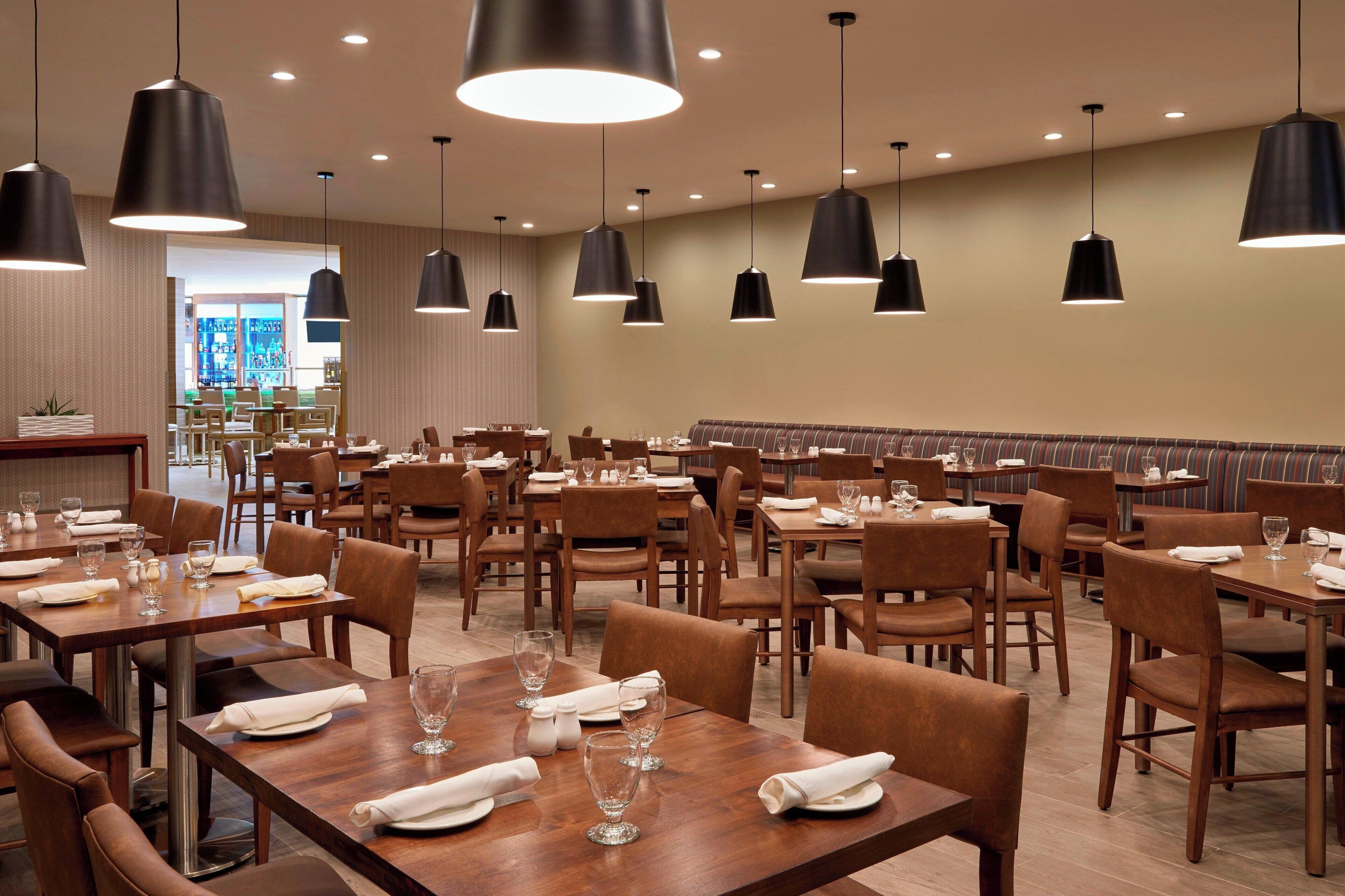A restaurant with multiple tables and chairs, black pendant lighting, and a view of the outdoor seating area.