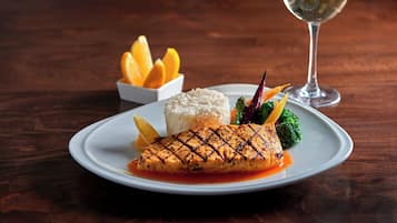 A plate of grilled salmon with rice and vegetables, accompanied by a glass of white wine on a wooden table.