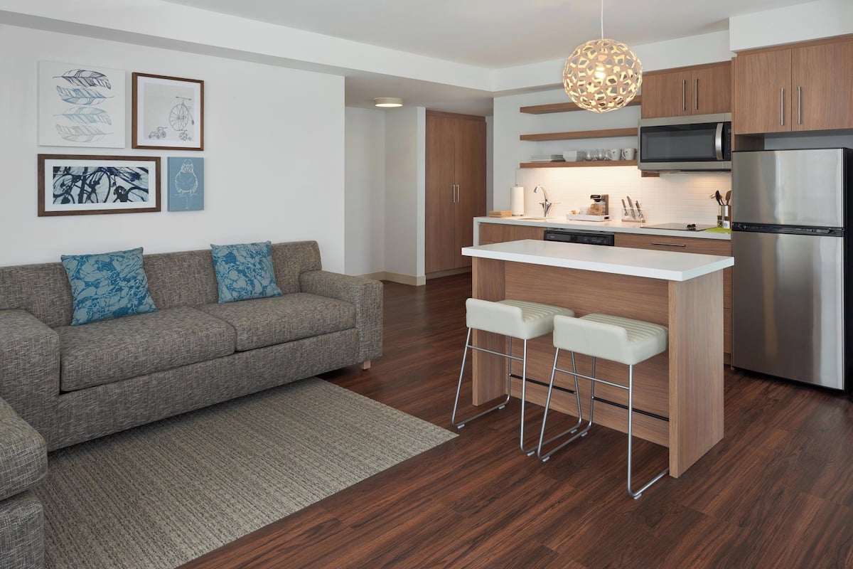 A modern kitchen with a central island, bar stools, and a stainless steel refrigerator.