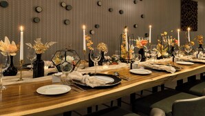 Una larga mesa de comedor dispuesta con velas, copas y centros de mesa florales.