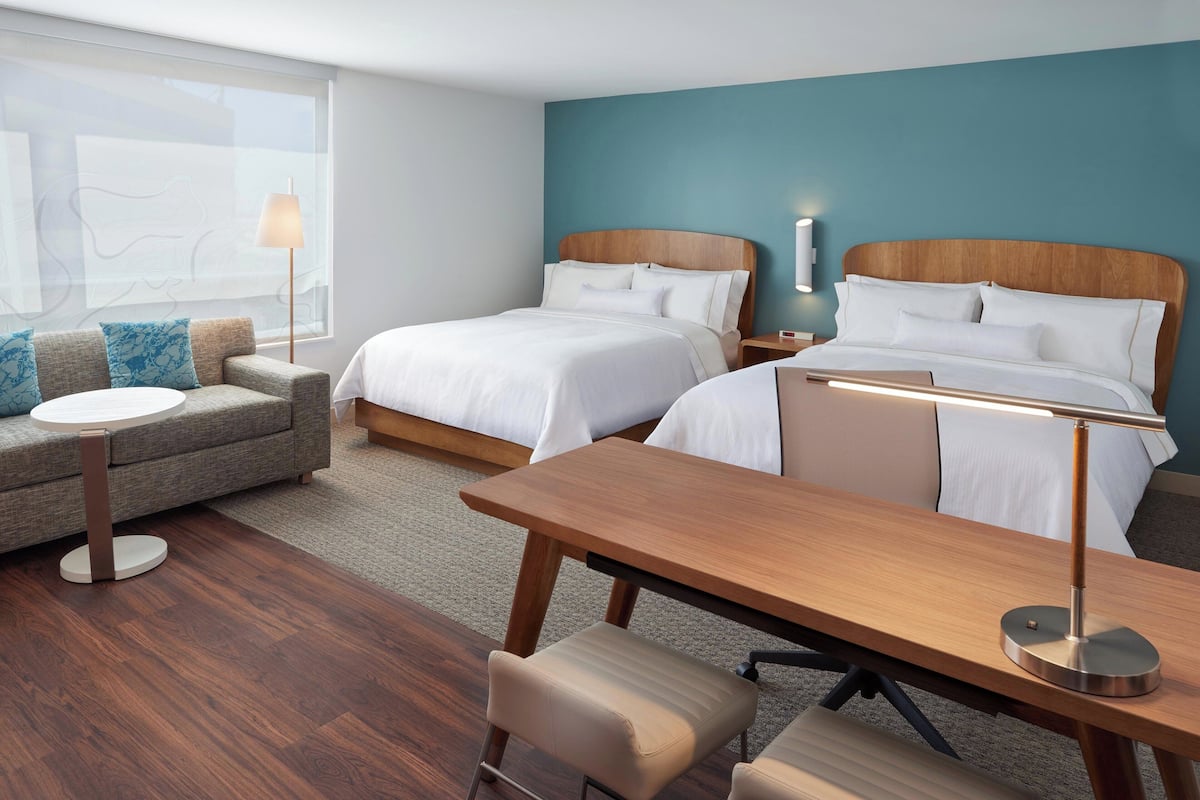 A hotel room with two beds, a sofa, a desk, and a lamp.