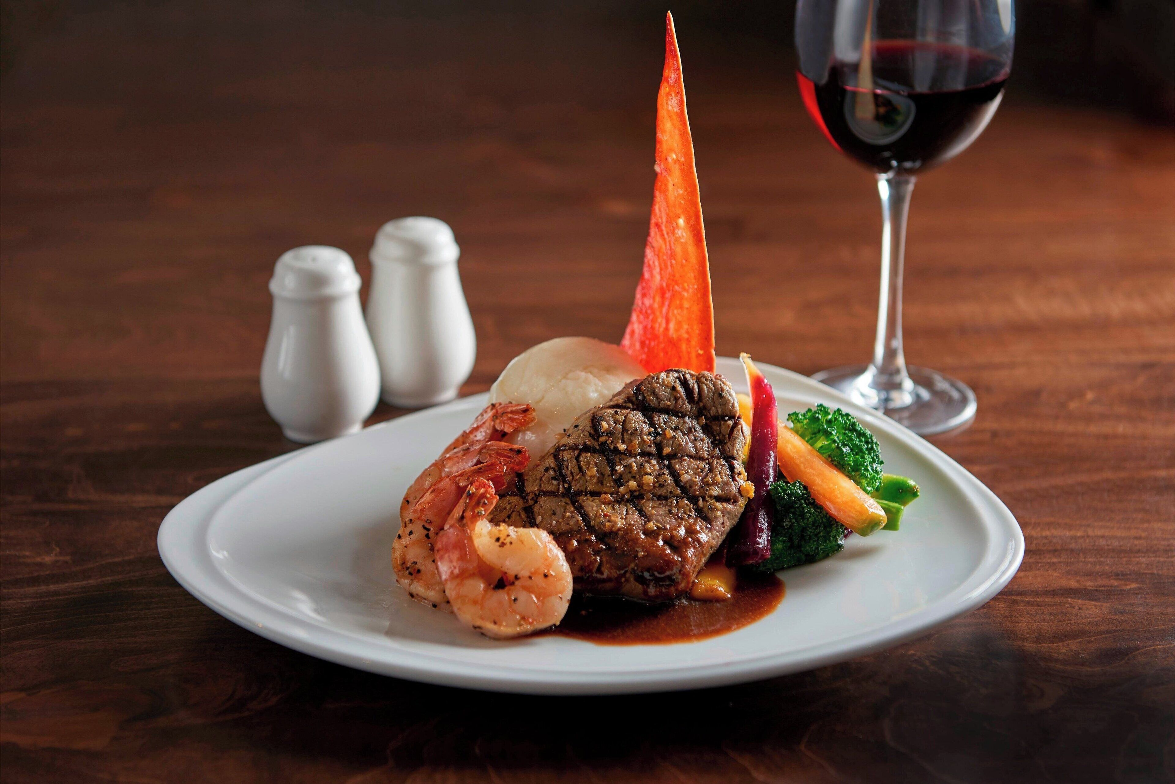 A plate of food with shrimp, steak, and vegetables on a wooden table.