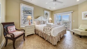 A bedroom with a bed, a chair, a nightstand, a ceiling fan, and a view of the outdoors.