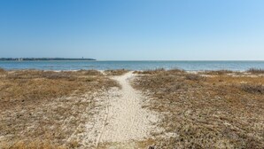 A sandy beach path leading to the ocean with a clear sky.
