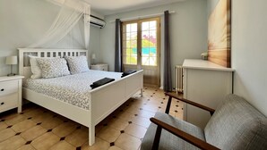 A bedroom with a bed, bedside tables, a chair, a window with curtains, and a painting on the wall.