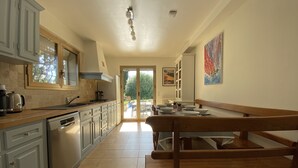 A spacious kitchen with a wooden bench, a dining table set for four, and a view of the garden through the sliding glass door.