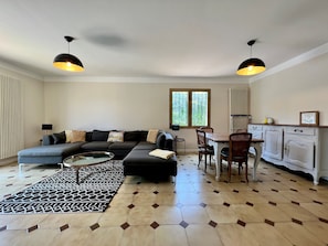 A modern living room with a sectional sofa, a dining table with chairs, and a kitchen area with cabinets.