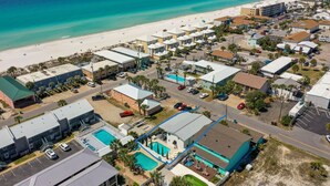 Luftaufnahme eines Küstenresorts mit mehreren Gebäuden, einem Strand und einem Schwimmbad.