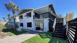 Ein modernes, zweistöckiges Haus mit überdachter Terrasse, Treppe und gepflegtem Rasen.