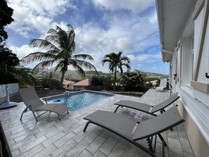 A pool area with lounge chairs, a small pool, and a view of a hilly landscape with palm trees. - Villa Vauclin 5 persons, calm and rest near the sea (LE VAUCLIN)