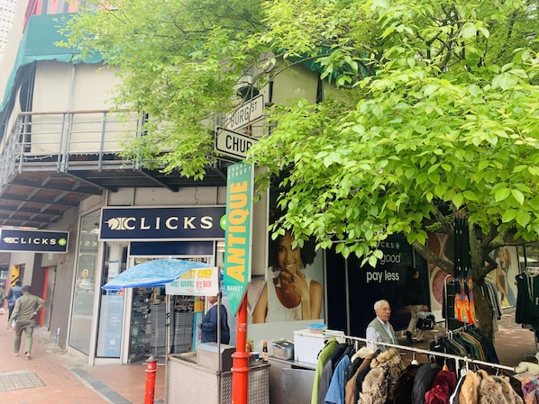 A street scene with a vintage market stall, a clothing rack, and a building with a sign that reads 'ANTIQUE MARKET'. - Stylish decorated and well positioned apartment in historical art deco building (Cape Town City Centre)