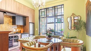 Una cocina con armarios de madera, un comedor con una mesa redonda y sillas, y un ventanal con vistas a edificios.