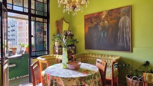 Un comedor con una mesa redonda, sillas, una araña, un cuadro y plantas en macetas.