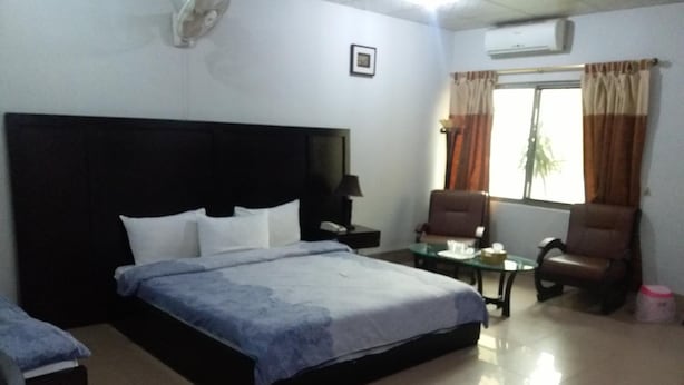 A hotel room with a large bed, two chairs, a small table, an air conditioning unit, and a window with curtains. - Amyls garden (Islamabad)