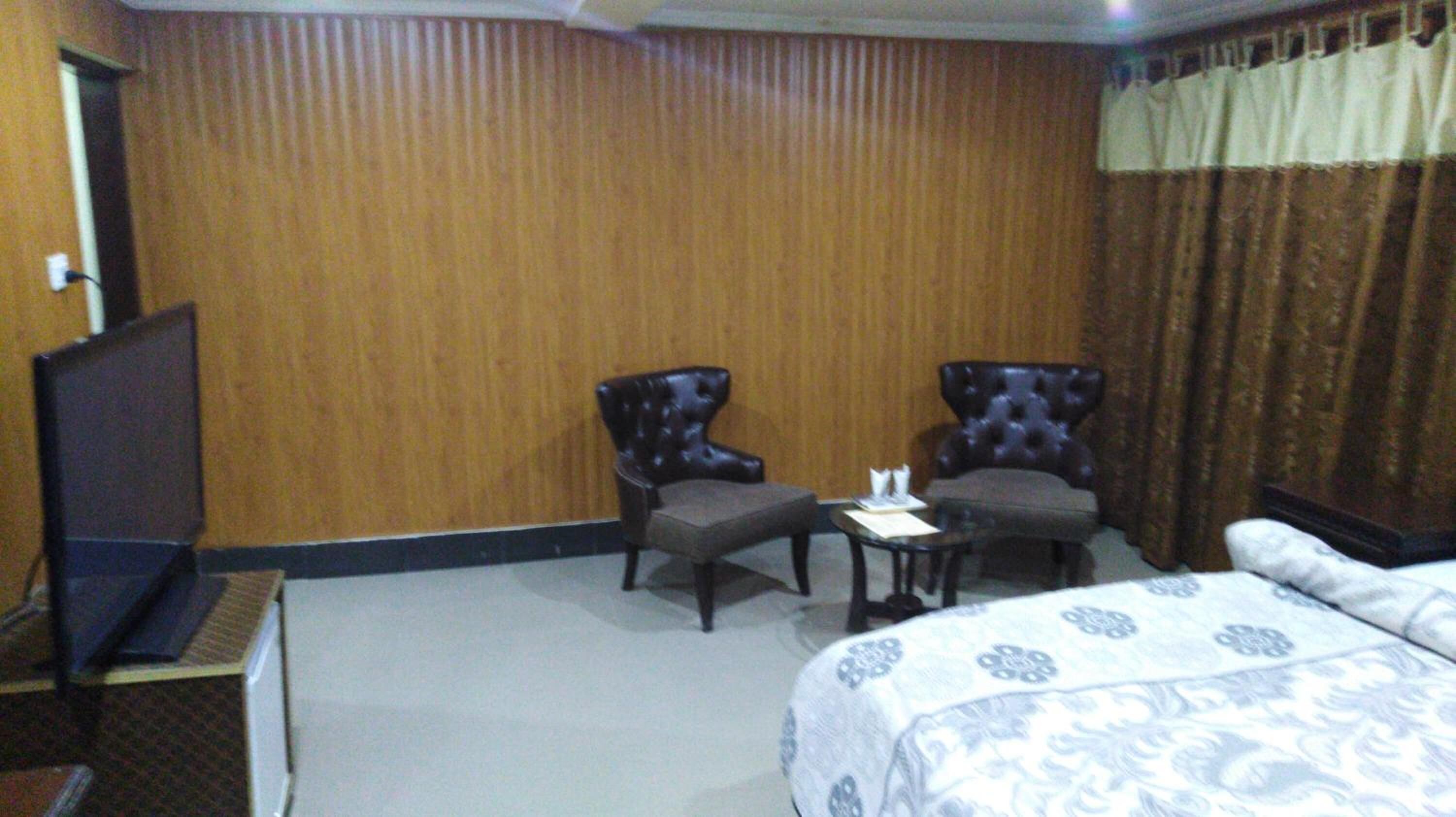 A hotel room with a bed, two armchairs, a small table, and a television.