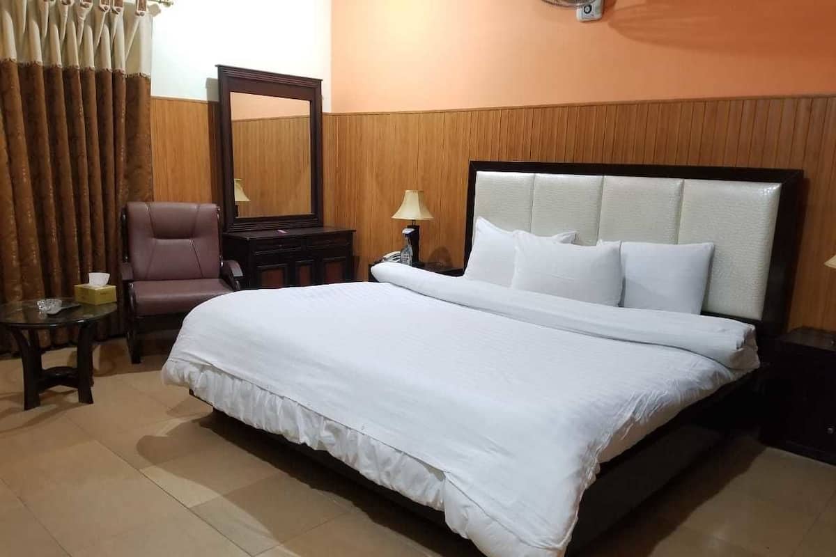 A neatly arranged hotel room with a large bed, a chair, a table, and a mirror.