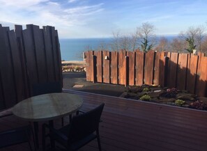 Una terraza con mesa y sillas, un cerco de madera y vistas al mar.