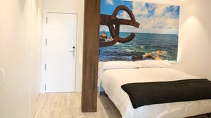 A bedroom with a bed, a white door, a wooden pillar, and a large painting of a sea scene with a rusted anchor. - Maddiola Apart 3, Orio (Orio)