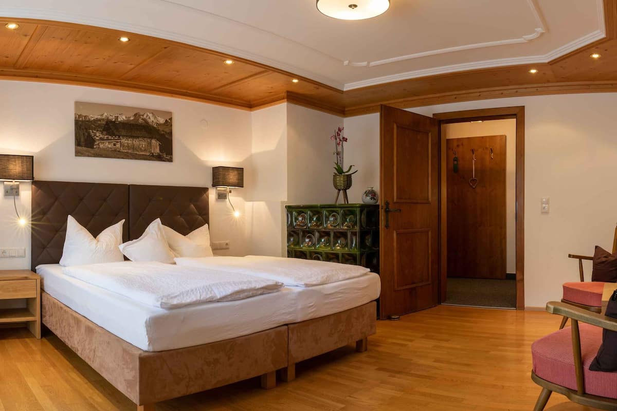 A bedroom with a large bed, two bedside tables, a wooden headboard, a wall-mounted shelf with decorative items, and a wooden door.