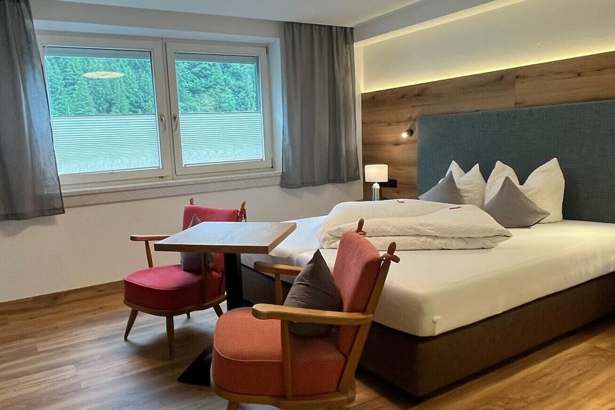 A hotel room with a bed, two chairs, a table, and a window with a view of greenery.