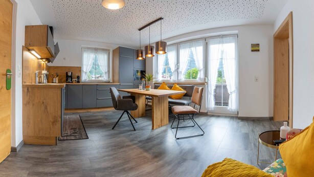 A modern kitchen with a wooden island, grey cabinets, and a dining area with a wooden table and chairs. - Apart Matthias (Mayrhofen)