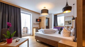 A modern hotel room with a bed, a desk, a chair, a potted plant, and a large window. - Apart Matthias (Mayrhofen)