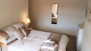 A neatly made bed with floral bedding, a bedside lamp, and a mirror on the wall. - Bright, spacious centrally-located 3-bedroomed house with ample free parking. (Stirling)