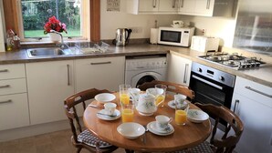 A kitchen with white cabinets, a gas stove, a microwave, and a sink. There is a dining table with plates, cups, and glasses of orange juice. - Bright, spacious centrally-located 3-bedroomed house with ample free parking. (Stirling)
