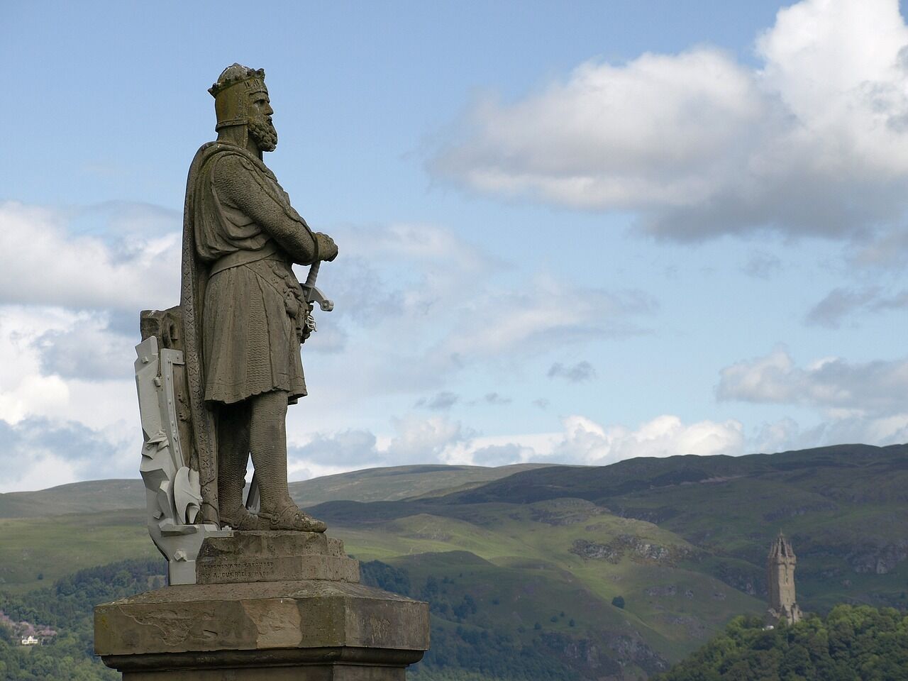 A stone statue of a historical figure on a pedestal, overlooking a landscape with rolling hills and a distant tower.