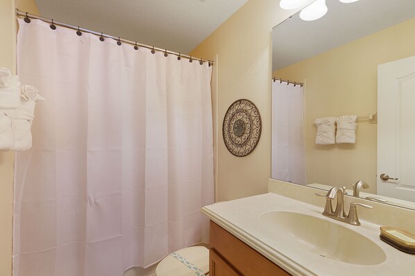 A bathroom with a shower curtain, a sink with a mirror, and a decorative wall plate.