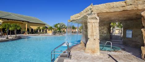 A swimming pool with a waterfall feature, a spa area, and a covered seating area with palm trees.