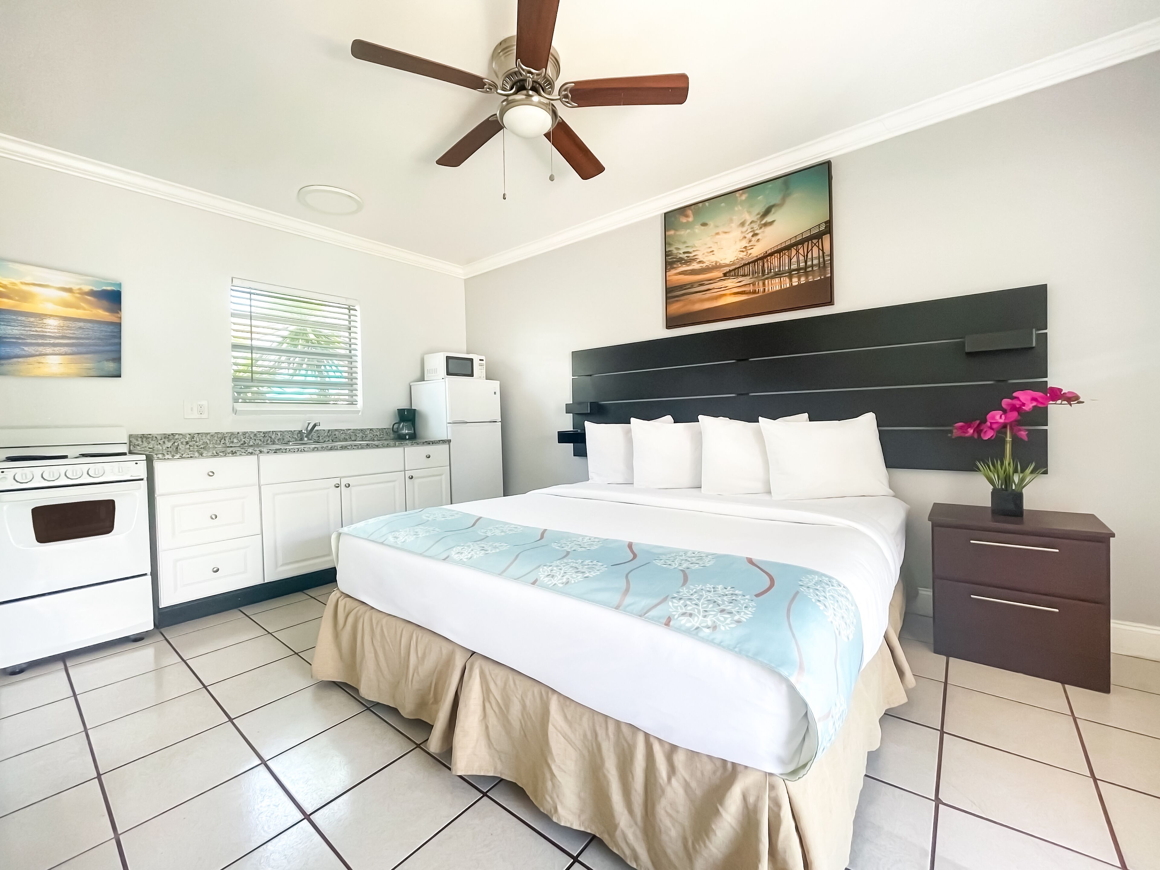 A hotel room with a bed, a desk, a microwave, a coffee maker, and a ceiling fan.