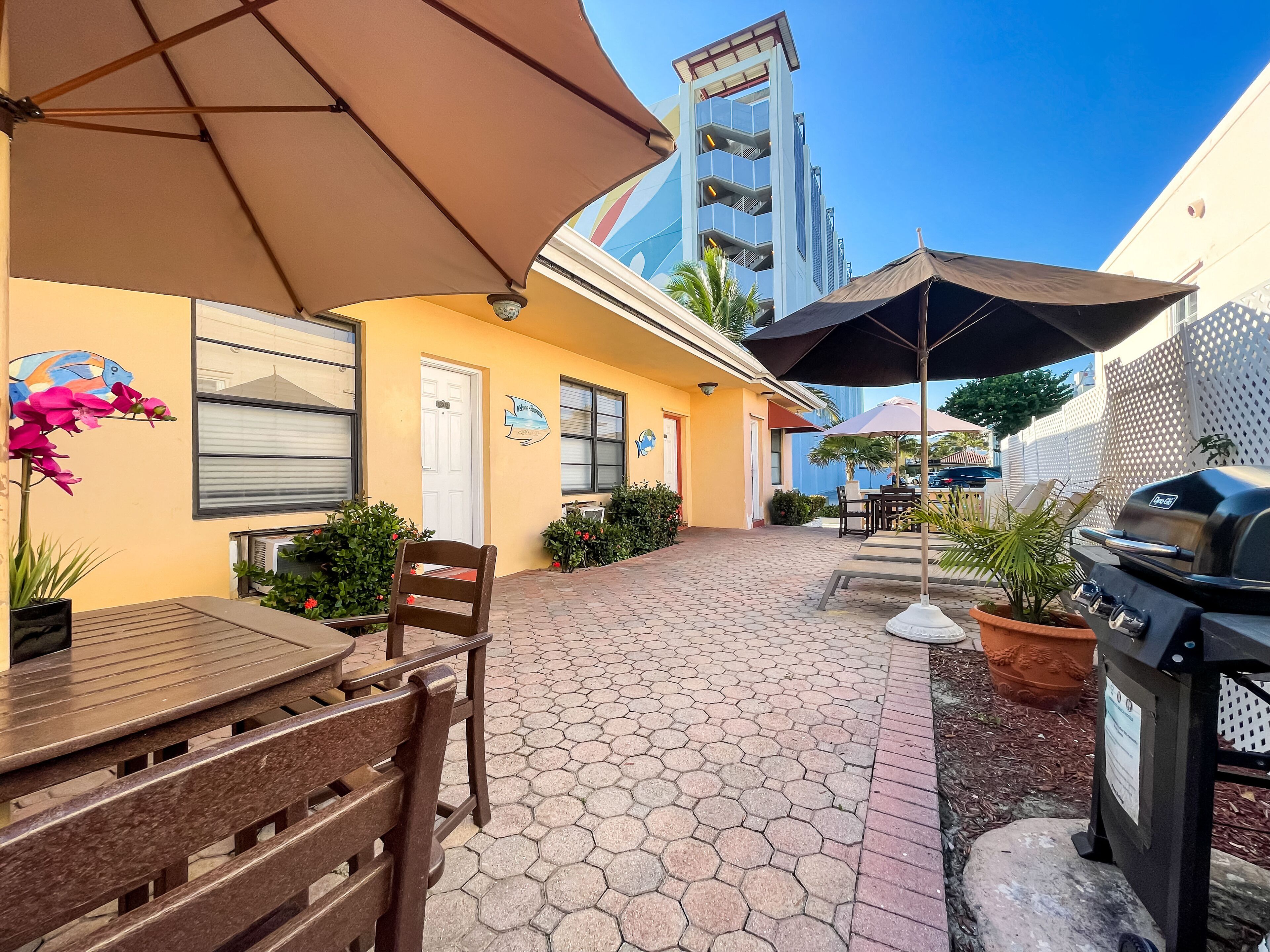 An outdoor patio with hexagonal tiles, a wooden table, chairs, and a barbecue grill.