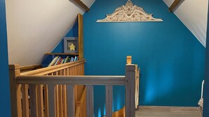 Una escalera con barandillas de madera que lleva a un rellano con pared azul y una lámpara decorativa en el techo.