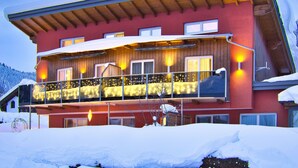 A multi-story building with a balcony, wooden exterior, and snow-covered surroundings. - Apartment Dahoam (Forstau)